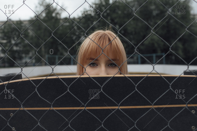 Portrait of young woman behind carver skateboard and wire mesh fence