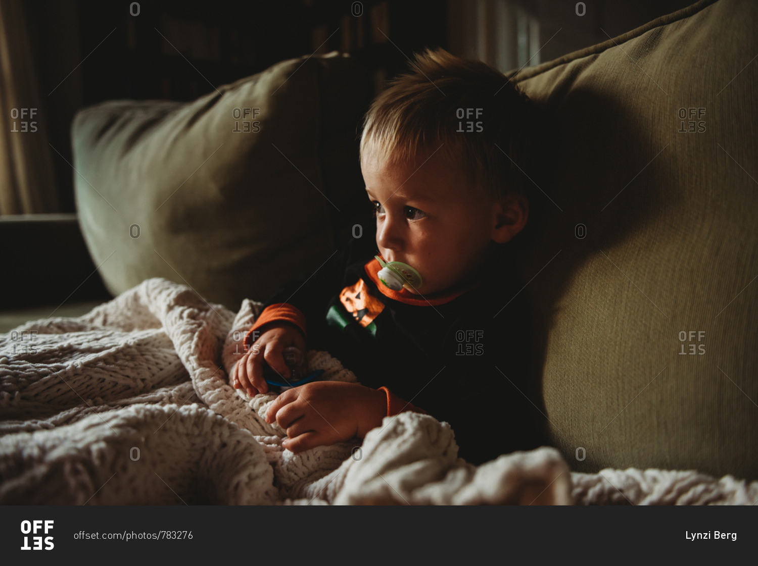 Toddler boy sitting on sofa with blanket and pacifiers stock photo OFFSET