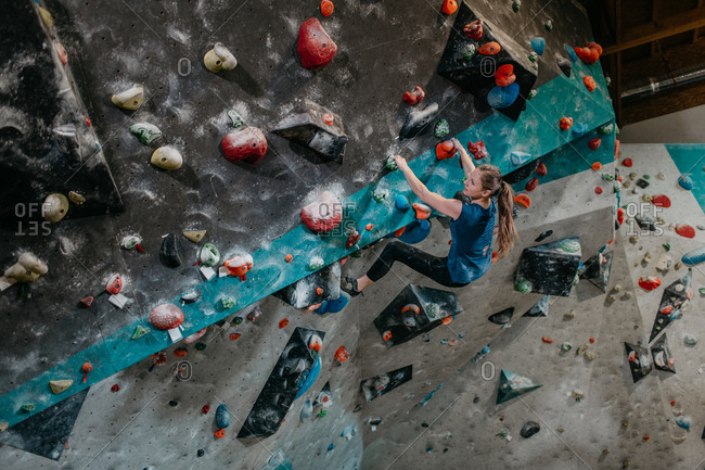 Woman climbing up an artificial climbing wall in an indoor bouldering gym. Female boulderer making her way up a bouldering wall.