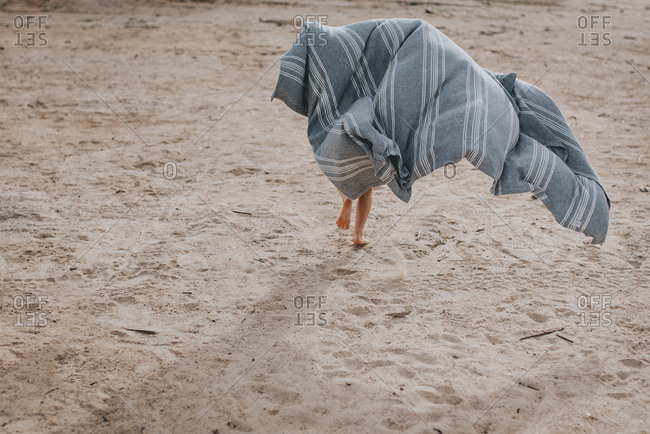 Child running with a blanket on a beach