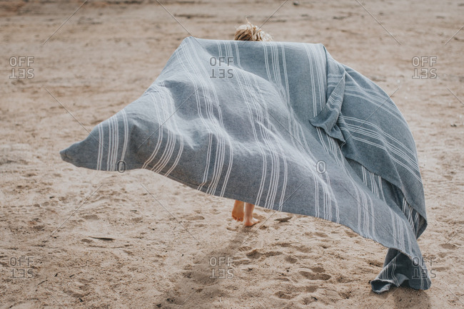 Young girl running with a blanket on a beach