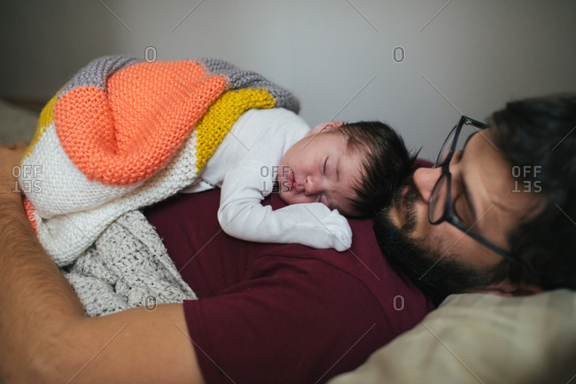 Sleeping newborn on dad's chest covered by blanket