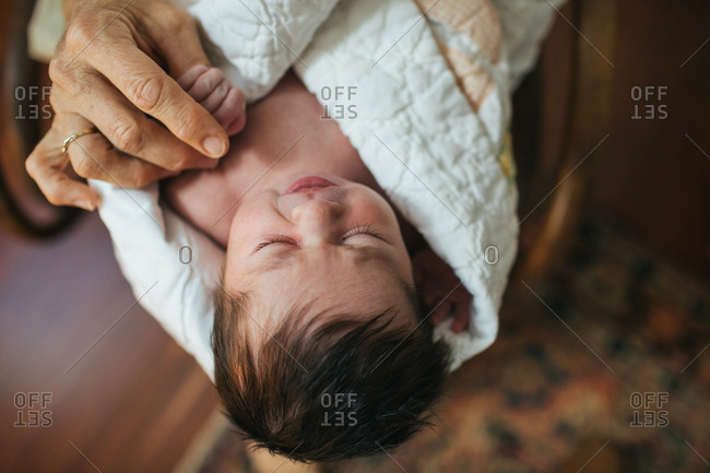 Close up of sleeping newborn in white blanket in grandmother's lap holding hand