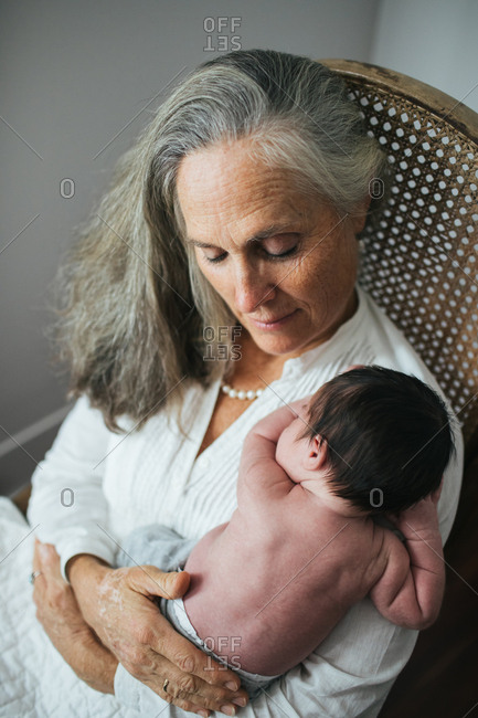 Smiling grandmother with long grey hair holding newborn in rocking chair