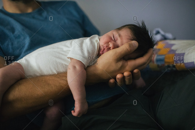 Sleeping newborn in dad's hand with quilt in background