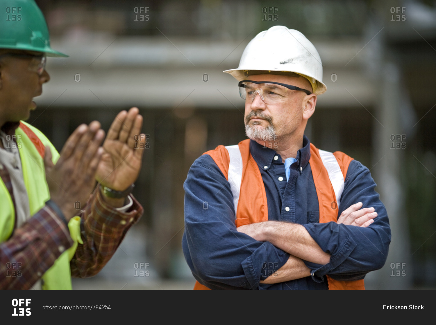 Mature male construction worker listening to a mid-adult male co-worker at a building site.