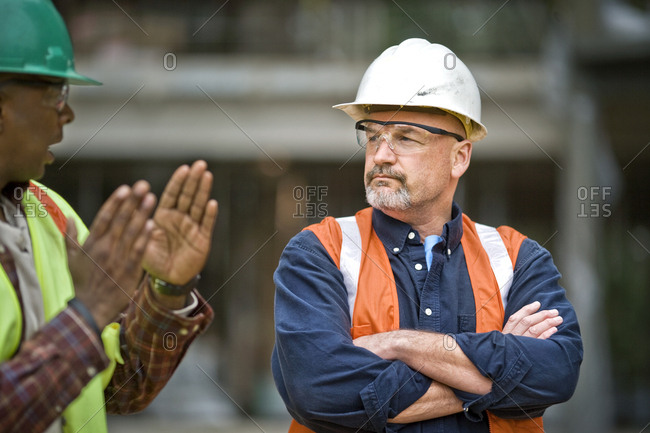 Mature male construction worker listening to a mid-adult male co-worker at a building site.