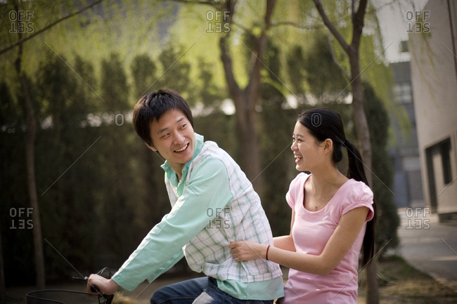 Young adult couple riding a bicycle along a park.