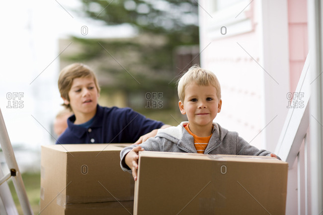 Young boy carrying boxes with his brother into a house.