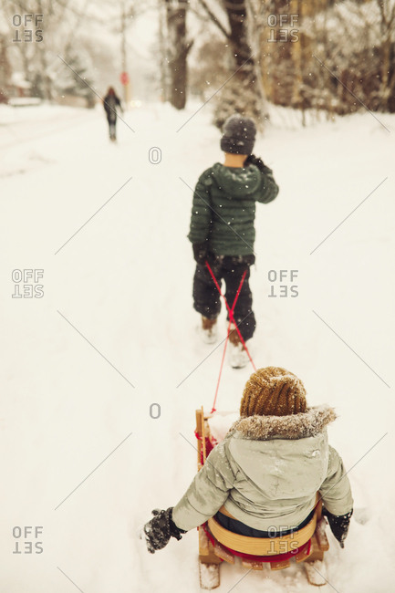 Older brother pulling sibling on a sled in a snow storm