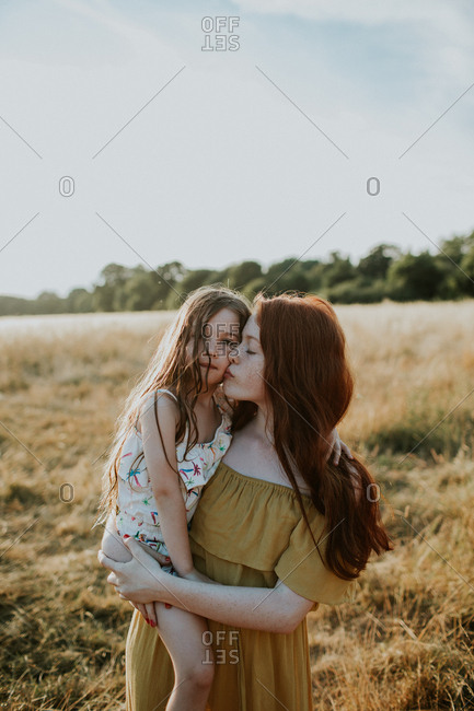 Girl giving her little sister a kiss on the cheek at sunset in a field