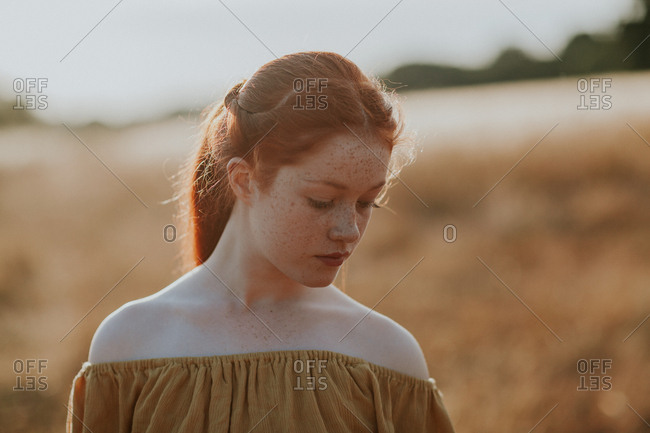Young redhead girl with freckles in a field at sunset