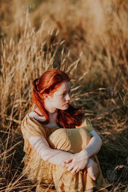Young redhead teen sitting in a field at sunset
