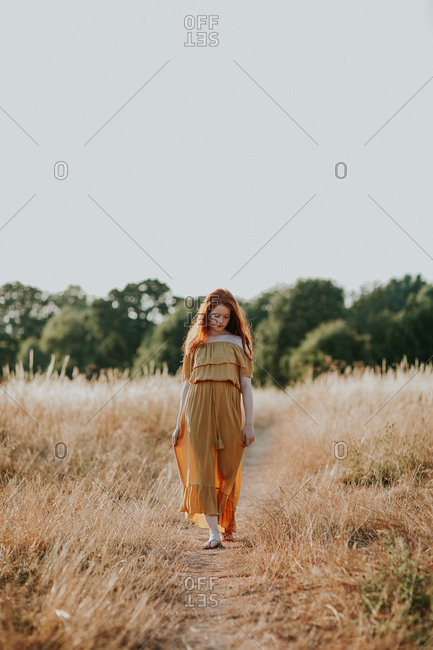 Beautiful teen with long red hair walking in a field at sunset