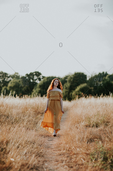 Beautiful teen with red hair walking in a field at sunset