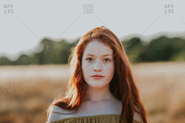 Portrait of a beautiful teen with red hair in a field at sunset