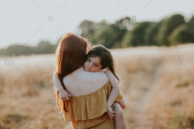 Girl carrying her little sister through a field at sunset