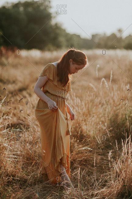 Beautiful teen with ginger hair walking in a field at sunset