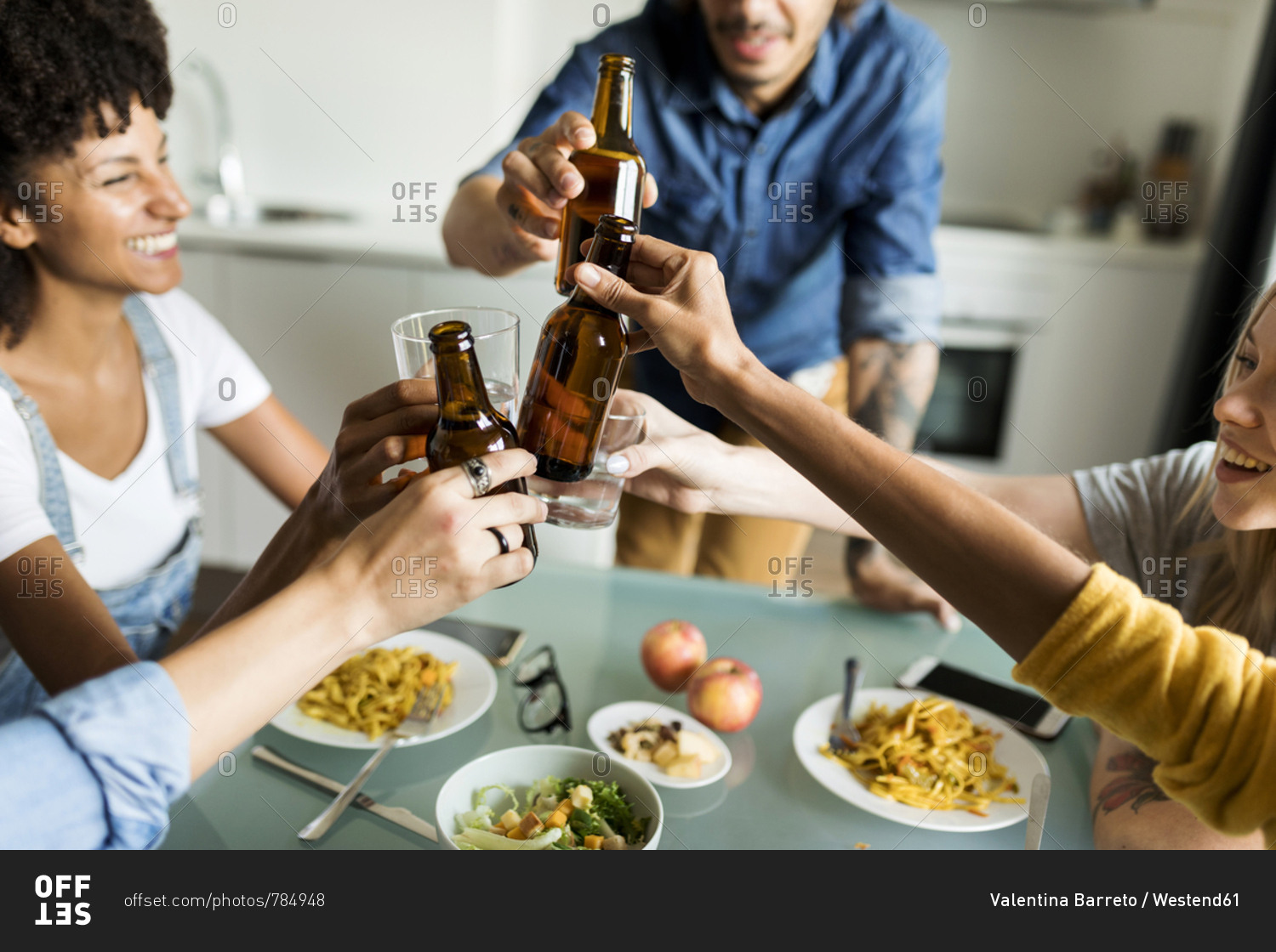Cheerful friends clinking beer bottles at dining table