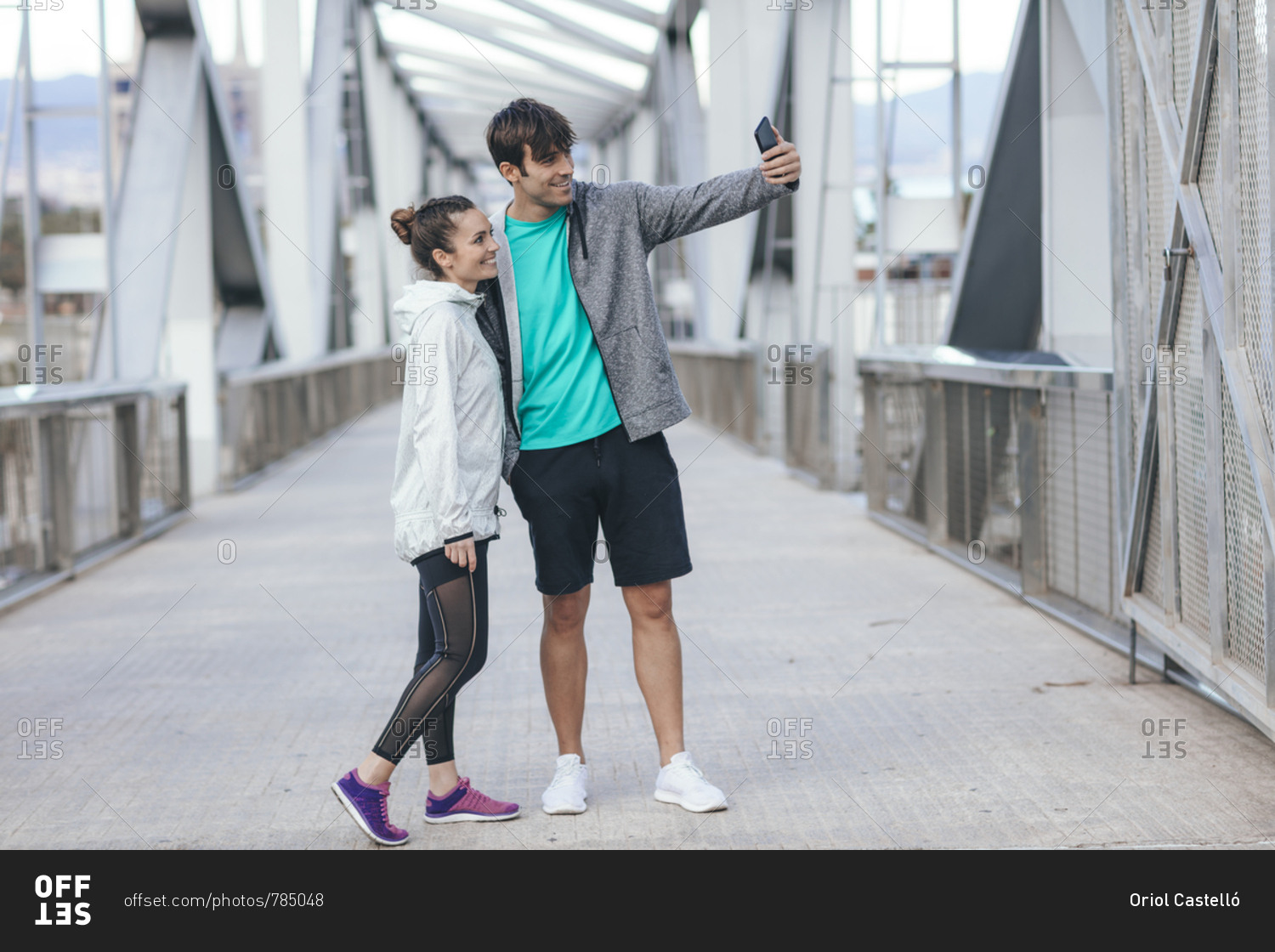 Young couple in athletic clothing taking a selfie on a bridge