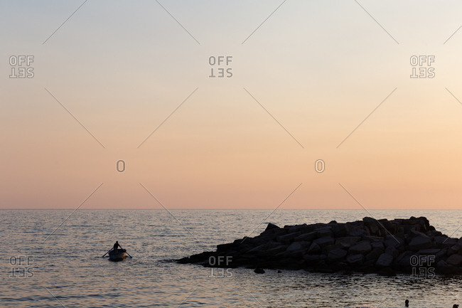 A man rowing a small manual boat out of a small fishing harbor in the South of Italy.