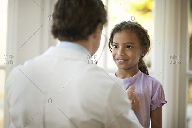 Middle aged doctor listening to a young patient's heartbeat with a stethoscope.