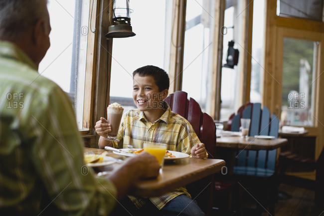 Boy with cream around his face grinning while sitting in a diner with his father.