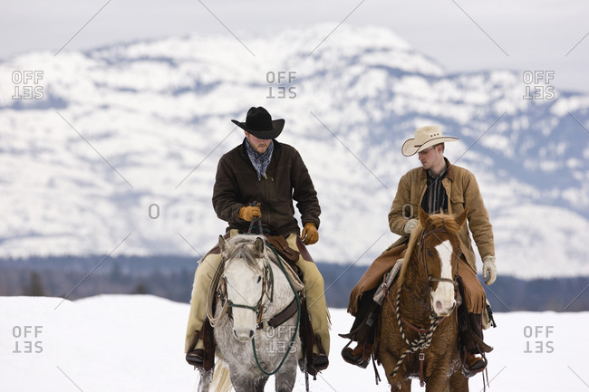 Two cowboys riding horses in a snow-covered countryside.