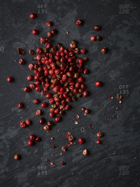 Whole pink peppercorns on a piece of slate shot form above, with some crushed pepper scattered about.