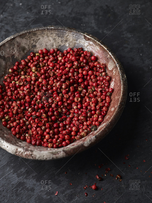 Whole pink peppercorns in a round pinch pot with some crushed on the surface and scattered about.