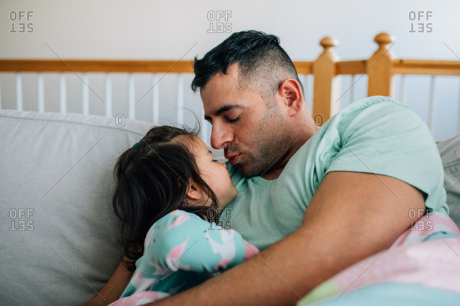 Father giving little girl a kiss in bed