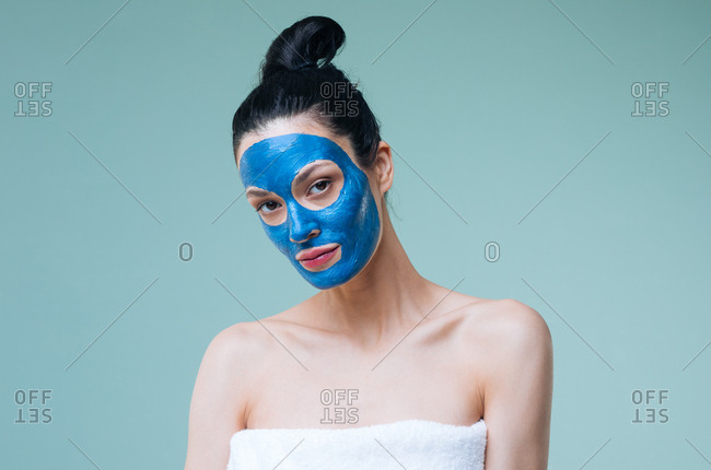 Portrait of pretty Caucasian woman brunette with blue clay cosmetic face mask looking at camera.