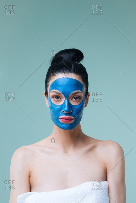 Studio portrait of beautiful Caucasian woman brunette with blue clay face mask looking at camera.