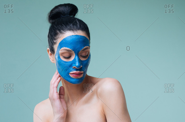 Portrait of beautiful Caucasian woman brunette with blue clay cosmetic face mask.