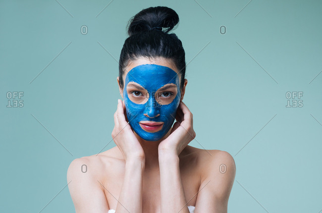 Portrait of pretty Caucasian woman brunette with blue clay cosmetic face mask looking at camera.