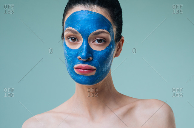 Studio portrait of beautiful Caucasian woman brunette with blue clay face mask looking at camera.
