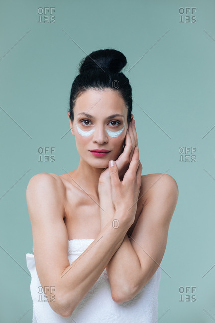 Studio portrait of beautiful Caucasian woman with cosmetic mask under her eyes and looking at camera.