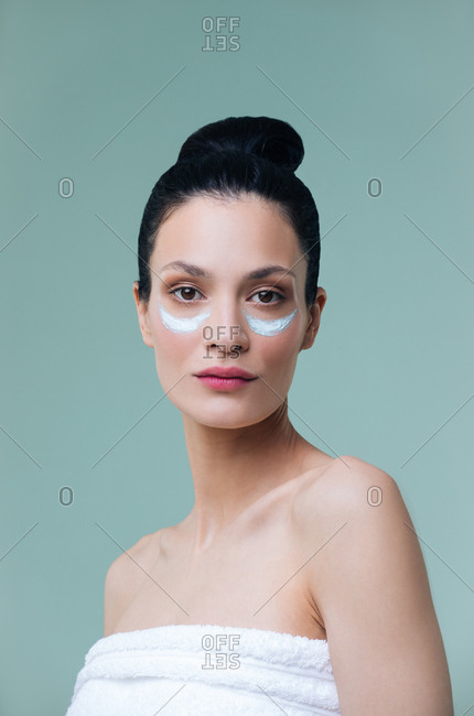 Studio portrait of beautiful Caucasian woman with cosmetic mask under her eyes and looking at camera.