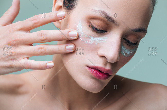 Close up of beautiful serious Caucasian woman putting cosmetic cream on her face.