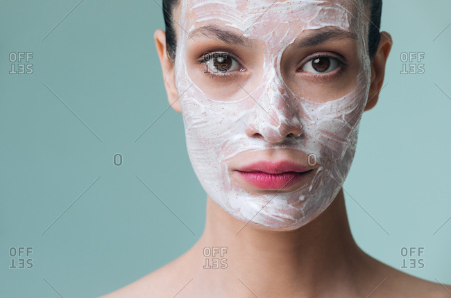 Beautiful Caucasian woman with cosmetic scrub cream on her face looking at camera.