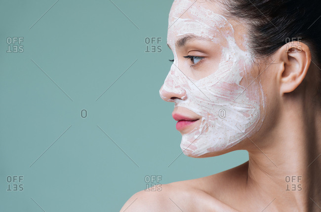 Beauty portrait of beautiful Caucasian woman posing with white cosmetic scrub cream on her face.