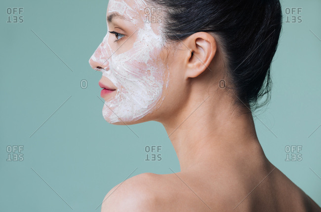 Beauty portrait of beautiful Caucasian woman posing with white cosmetic scrub cream on her face.
