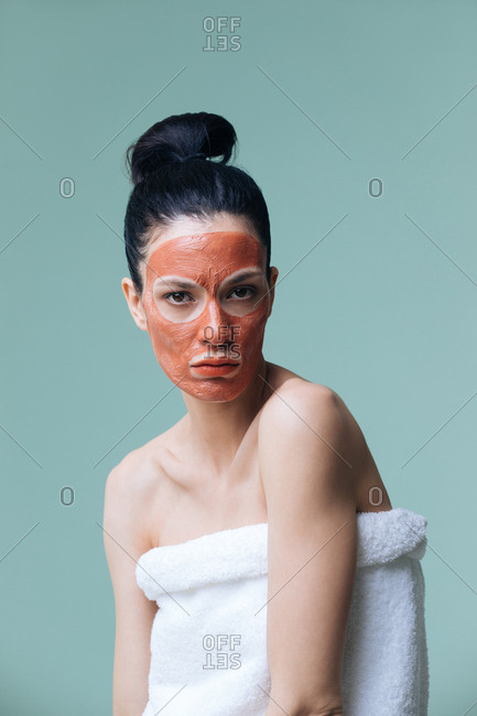 Beauty portrait of woman model posing with orange clay face mask on her face and looking at camera.