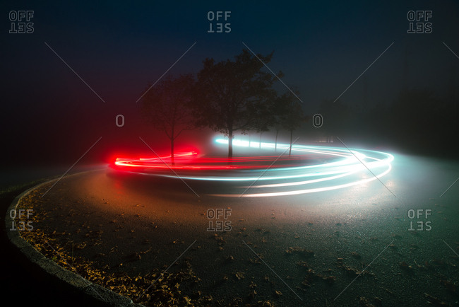 Abstract view of bright lines of lights on route between trees and mist in evening in countryside