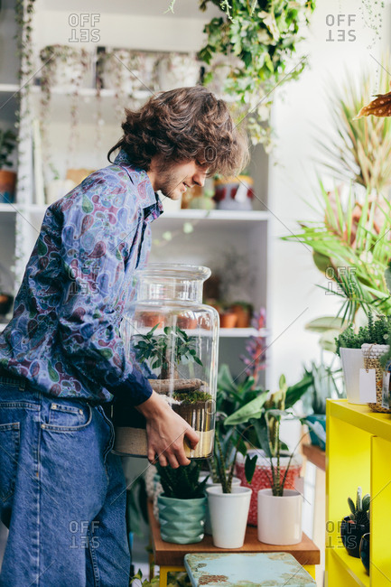 Man carrying plants in glass container in the flower shop. Small business, florist, retailing, work.