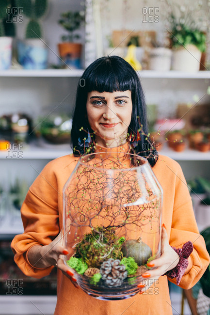 Woman holding plants in glass container in the flower shop. Small business, retailing, work.