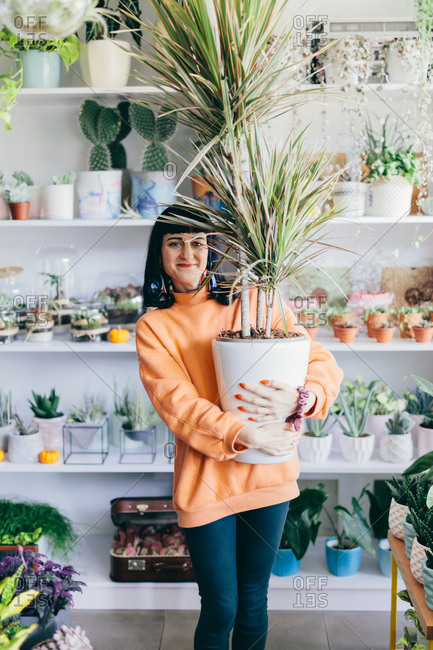 Woman holding big plant in flower pot. Flower shop, florist. Small business, retailing, shopping.