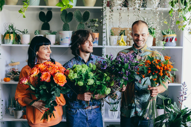 Woman and two men holding flower bouquets in the flower shop. Small business, creative occupation. Teamwork.