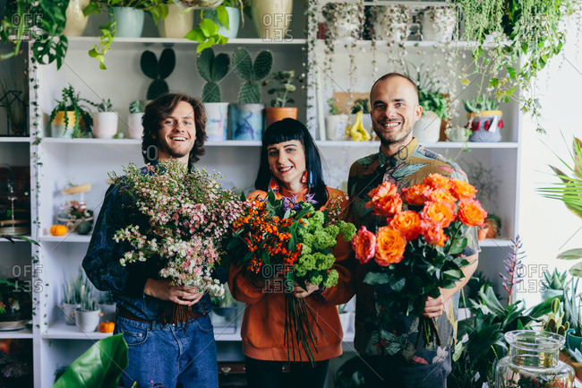 Woman and two men holding flowers in the flower shop. Small business, creative occupation. Teamwork.