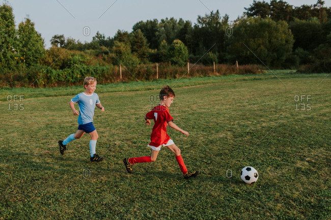 Children running after soccer ball. Full length of cheerful boys in football dresses chasing ball on football pitch.